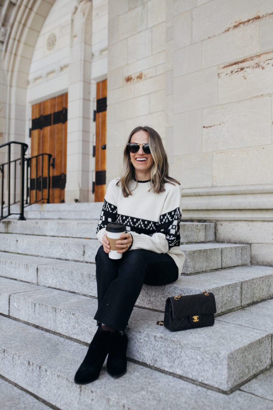Woman wearing black and white Christmas Fair Isle sweater with black jeans, black booties and Chanel purse