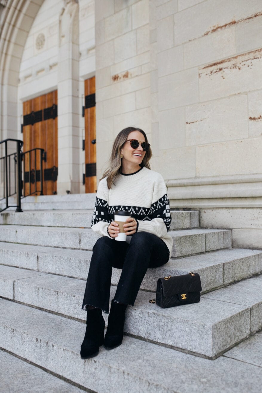 Woman sitting on steps wearing a black and white Fair Isle sweater with black pants and boots