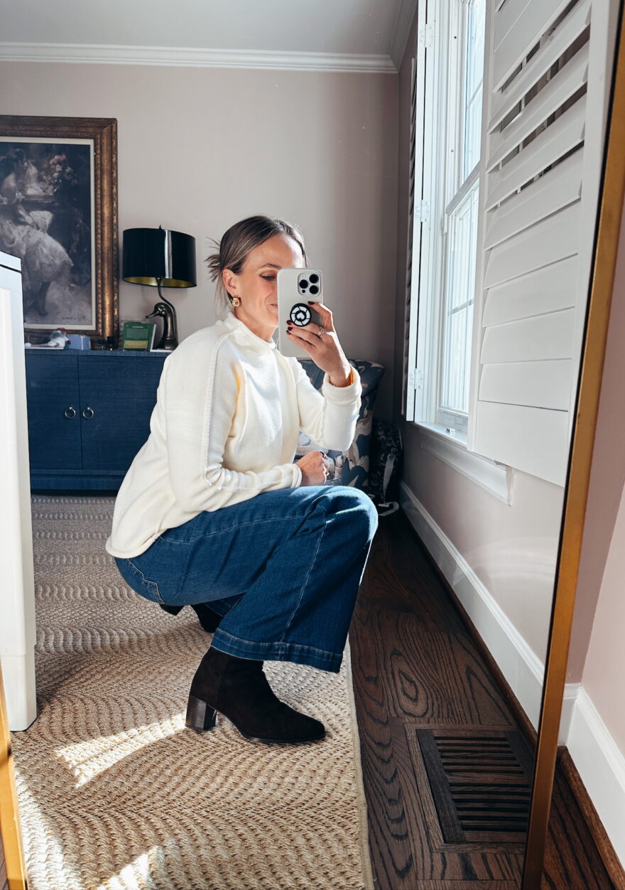 Woman taking selfie in denim jeans, ankle boots, and a white sweater