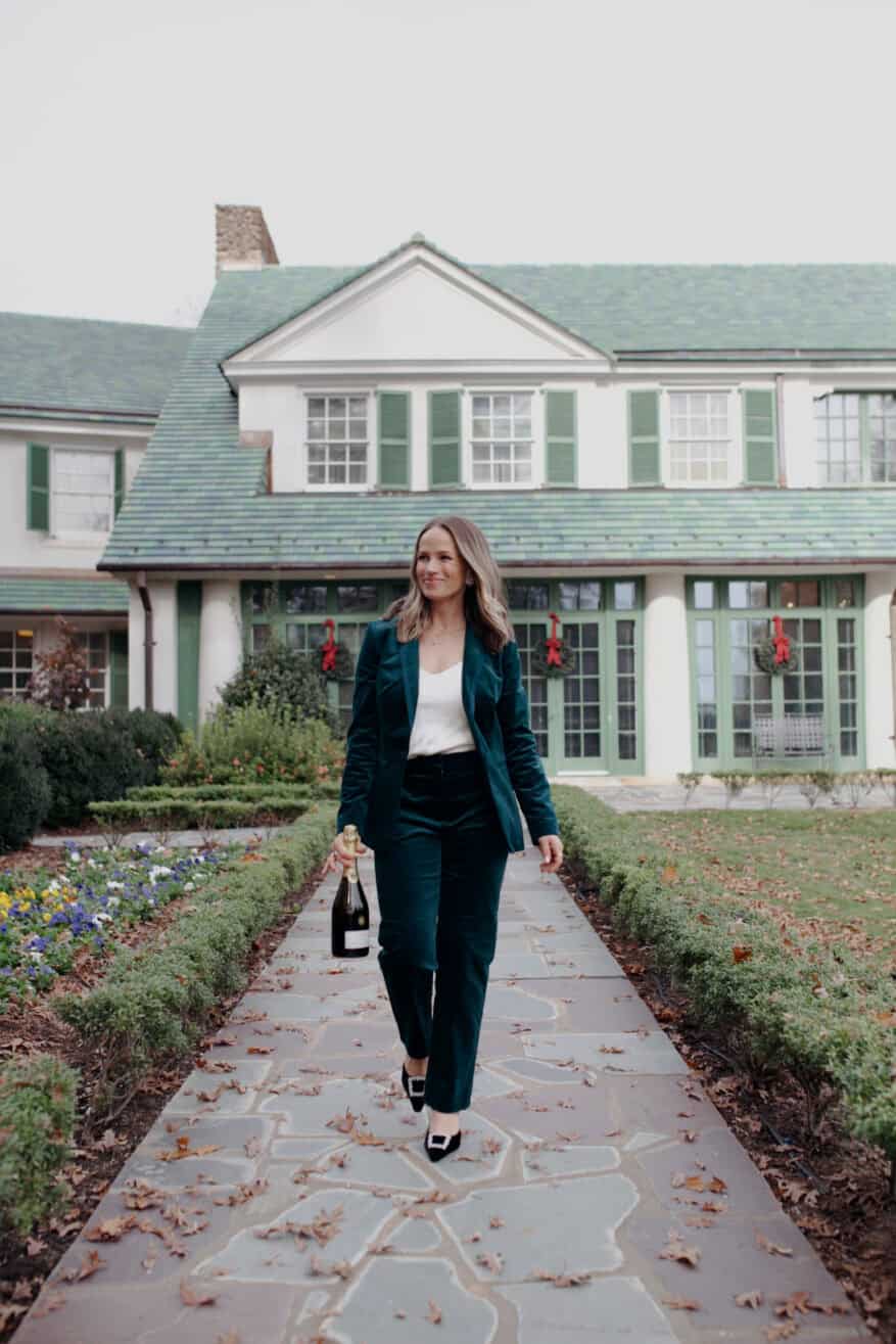 Woman wearing a velvet suit and carrying champagne while walking outside