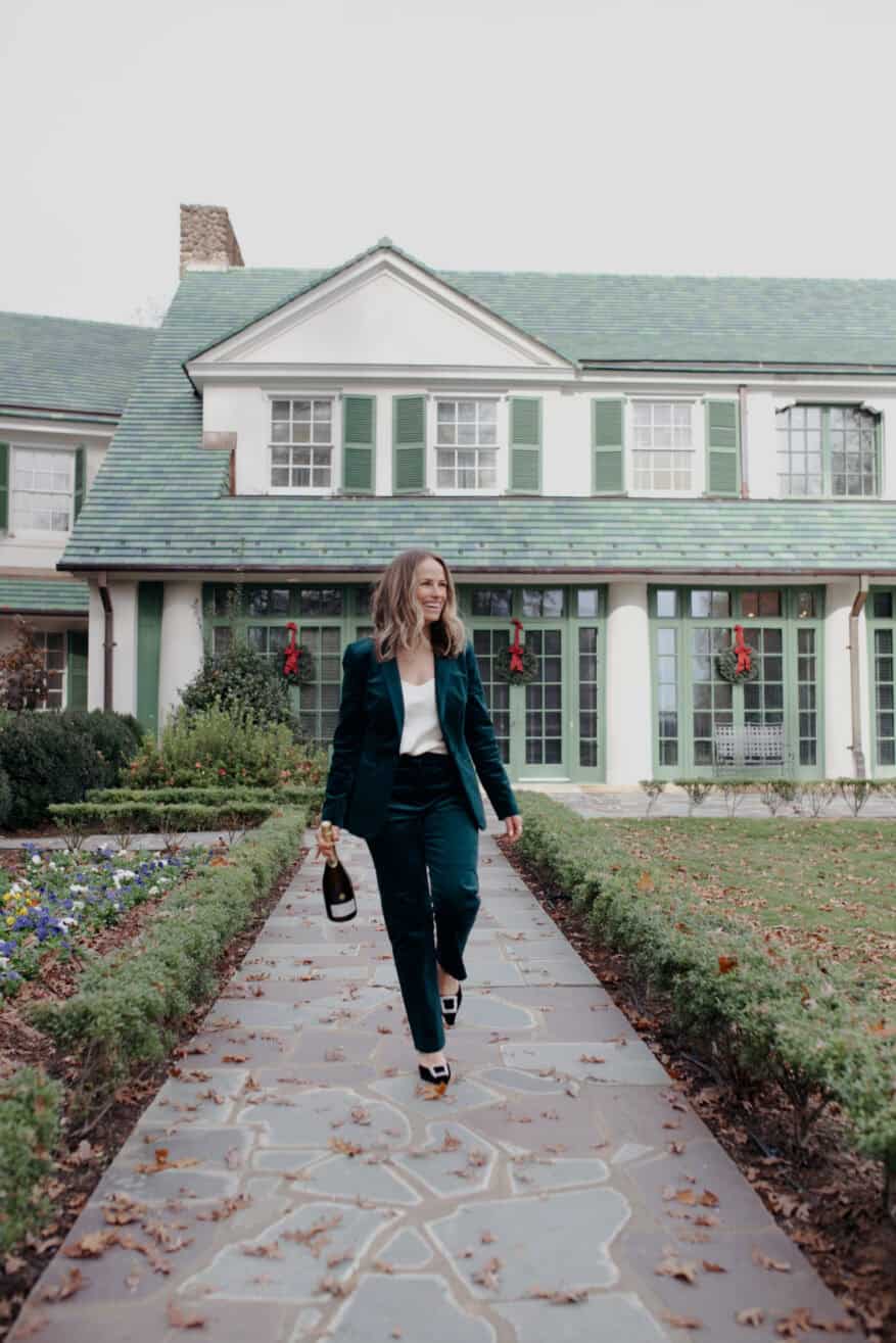 Woman wearing a green velvet suit and carrying champagne while walking outside