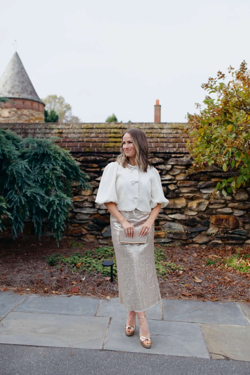 Woman wearing puff sleeve bow lady jacket from Anthropologie and the sequin midi skirt is by Ann Mashburn