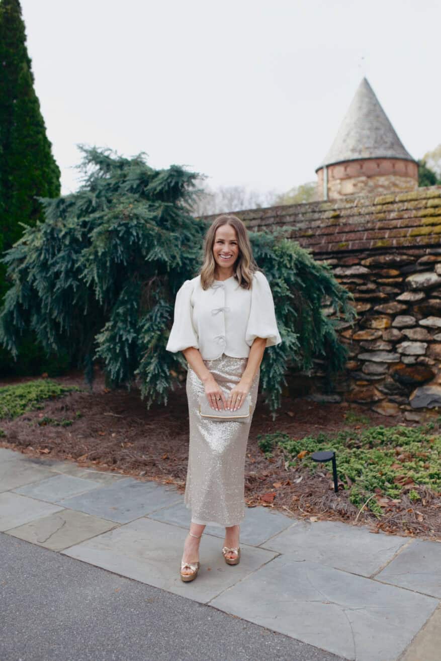 Woman wearing puff sleeve bow lady jacket from Anthropologie and the sequin midi skirt is by Ann Mashburn.