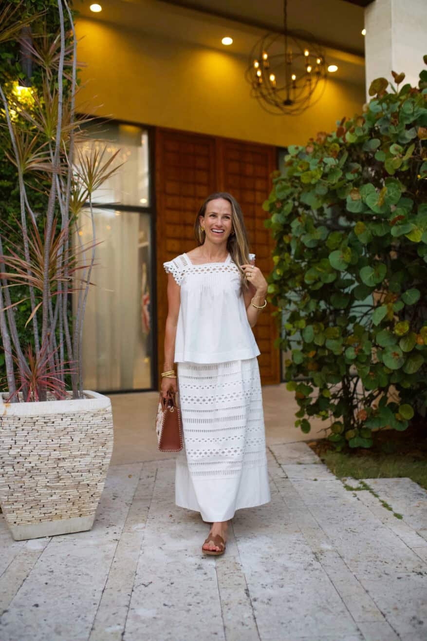 Woman wearing white cotton eyelet blouse and skirt while standing near bushes
