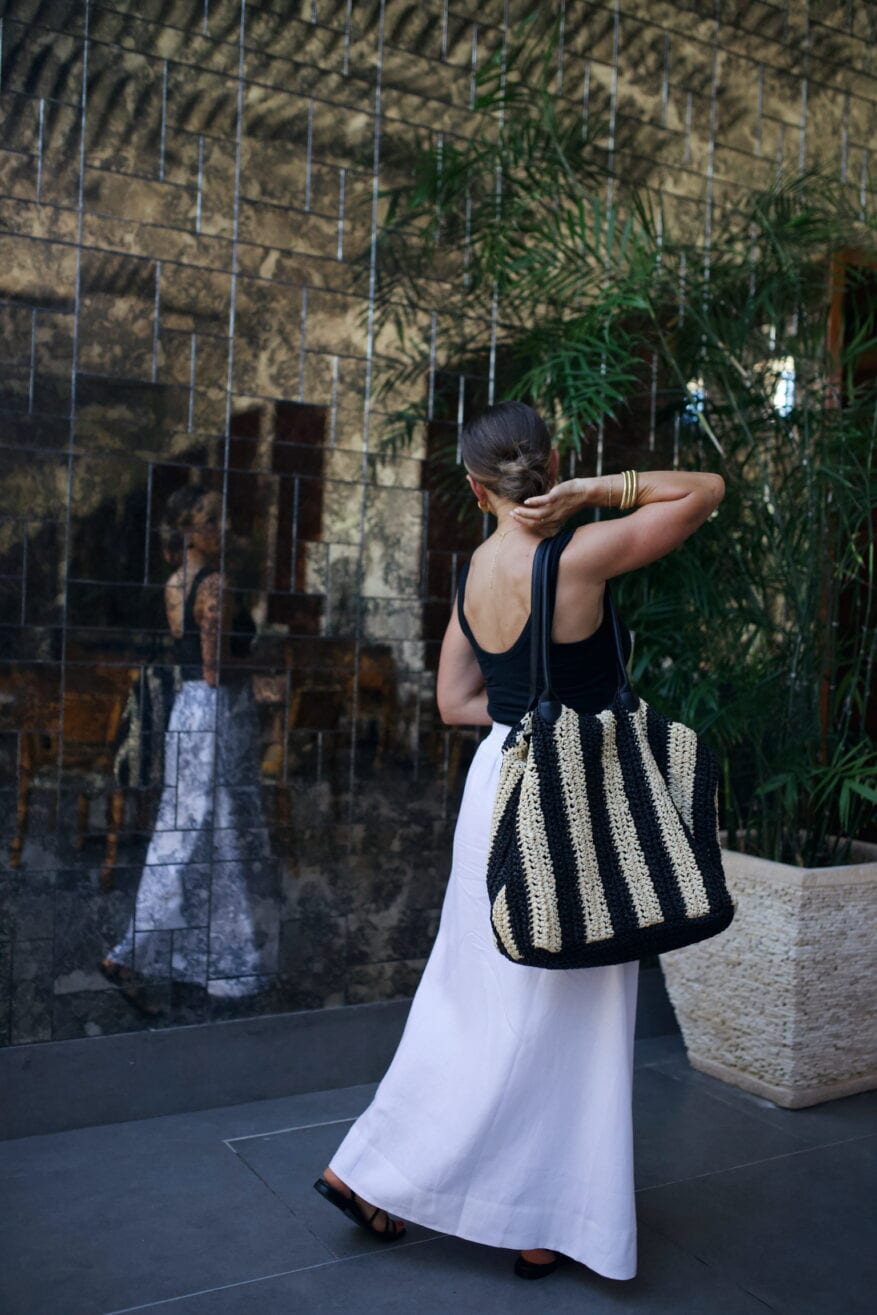 Woman wearing white skirt and black top with striped bag while walking at resort