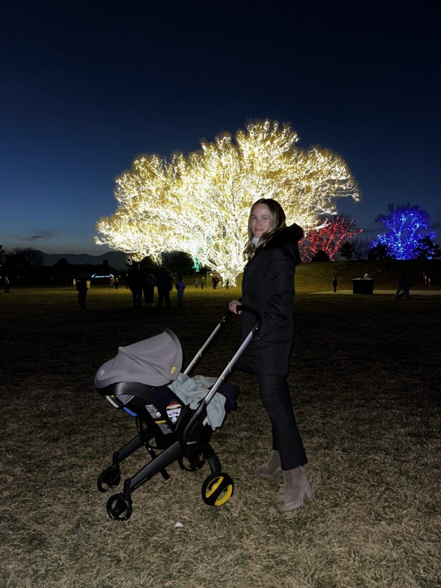 TeriLyn Adams pushing Doona stroller at night near lit-up holiday trees