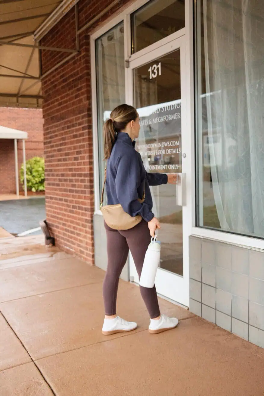 Woman walking into pilates class wearing leggings, jacket, and tennis shoes