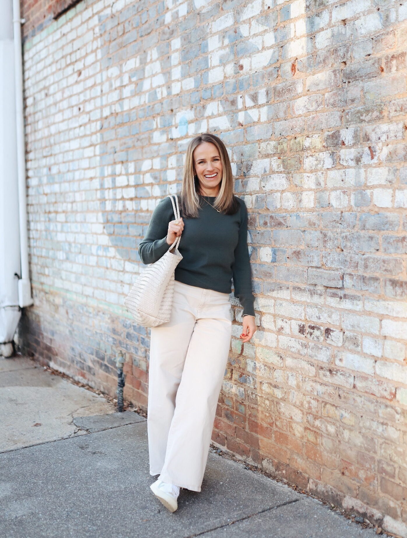 Woman wearing Quince top and pants while leaning on wall