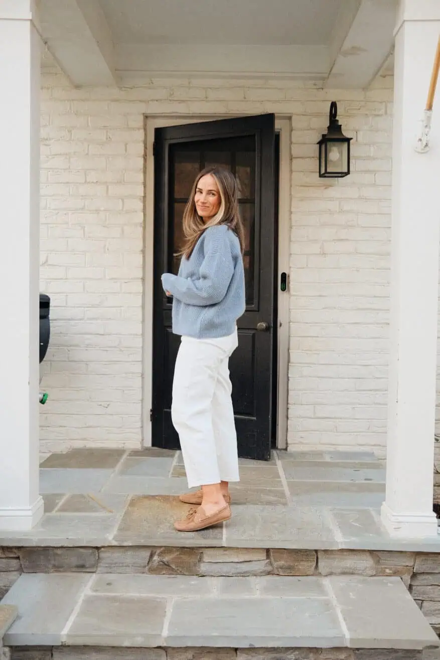 Woman standing on porch wearing white barrel jeans with blue sweater