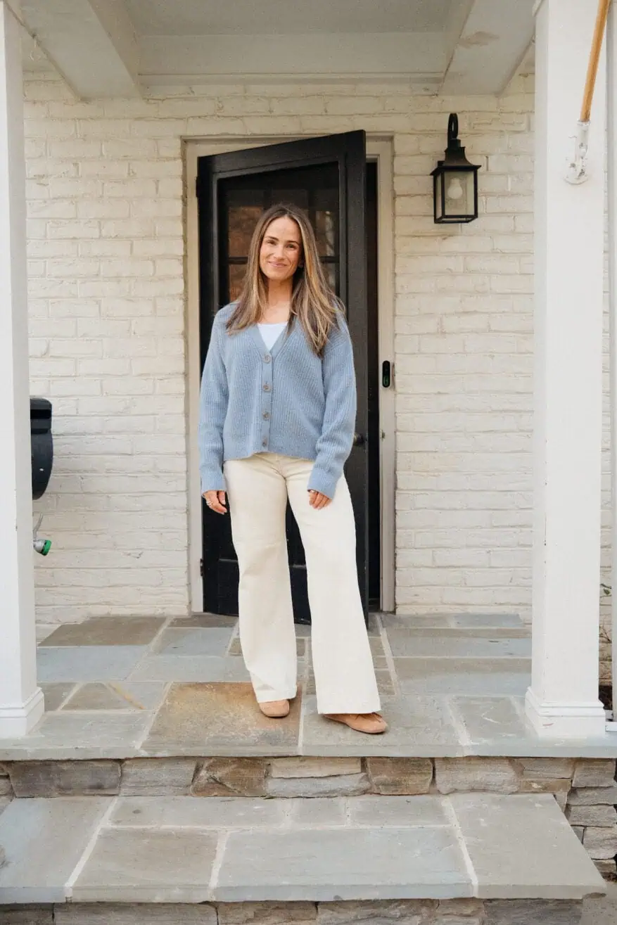 Woman standing on porch wearing white jeans and a blue button up sweater
