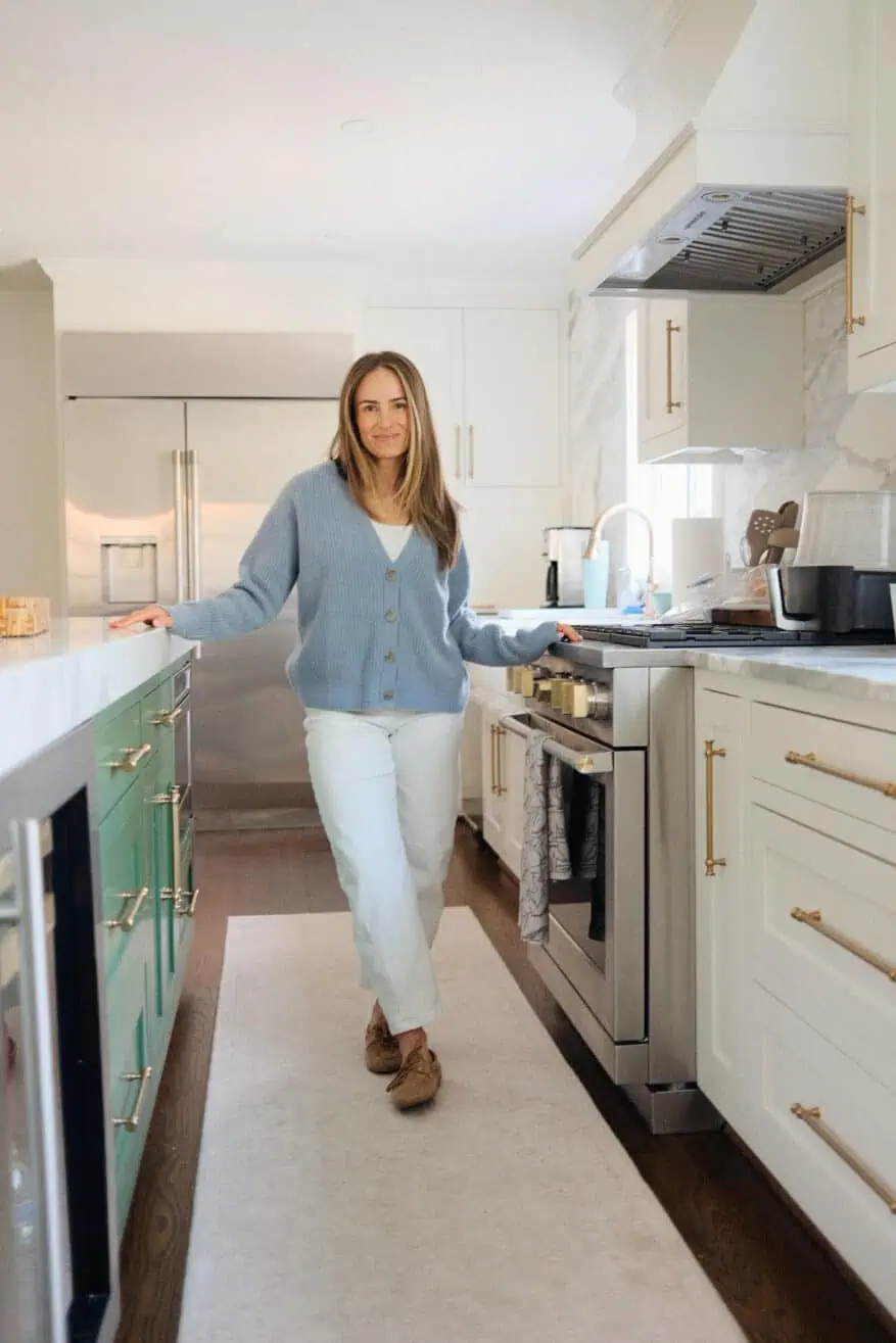 Woman standing in kitchen wearing white pants and a blue button up sweater