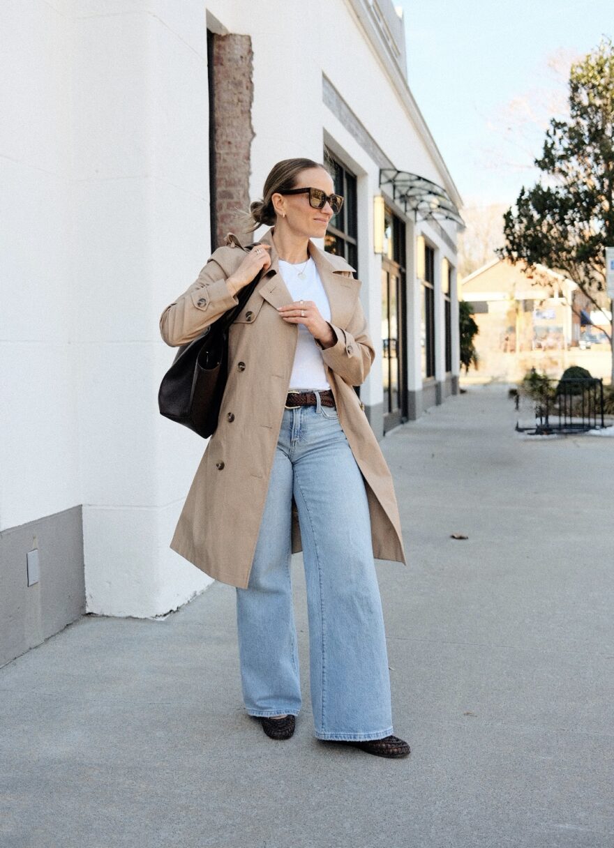 Woman standing outside wearing light blue jeans and a trench coat