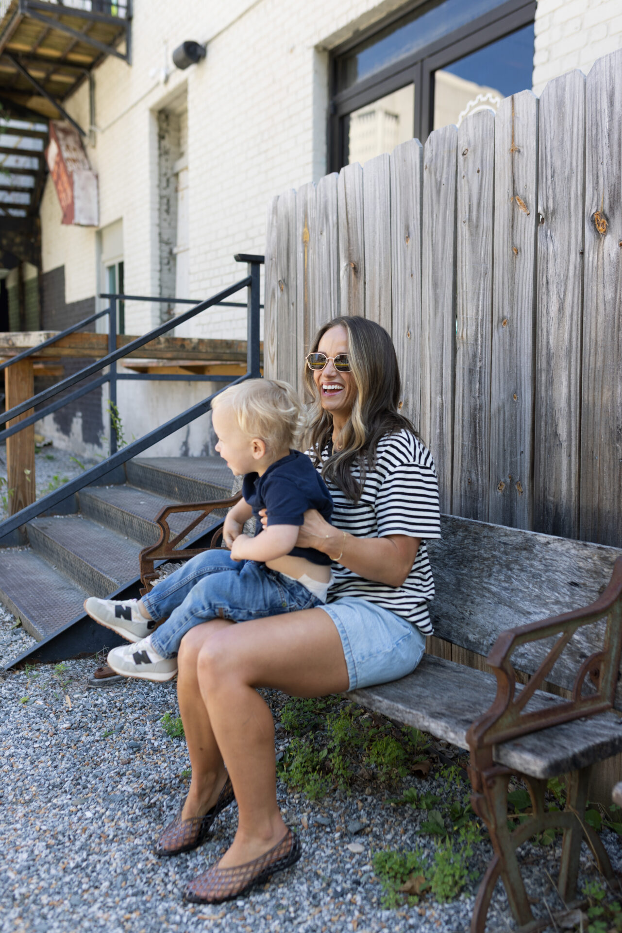 TeriLyn Adams holding toddler on bench wearing Abercrombie lose shorts and stripe tee with jelly shoes.