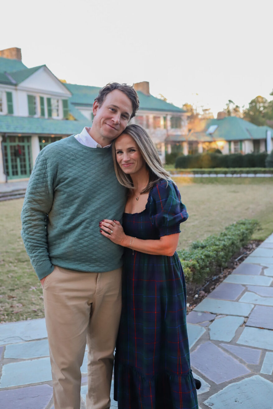 TeriLyn Adams in Hill House Louisa navy plaid dress holding baby while husband carries toddler on shoulders outside estate