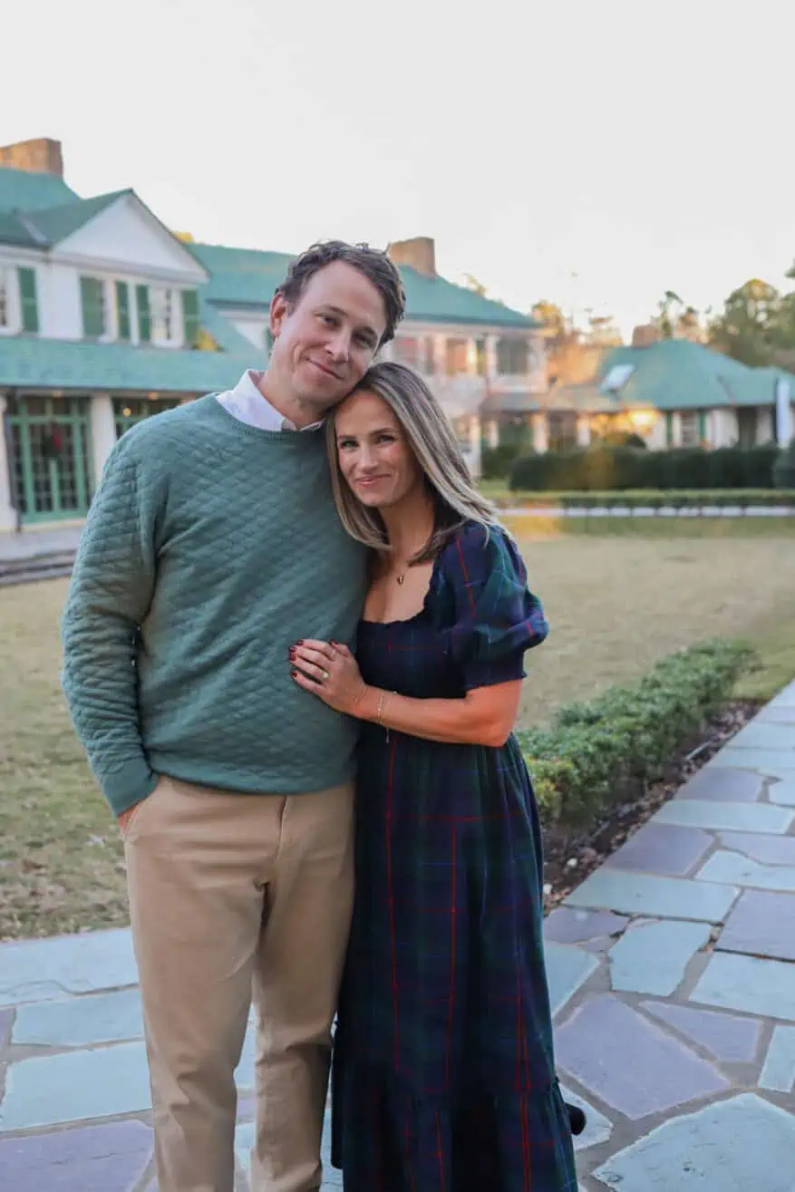 TeriLyn Adams in Hill House Louisa navy plaid dress holding baby while husband carries toddler on shoulders outside estate