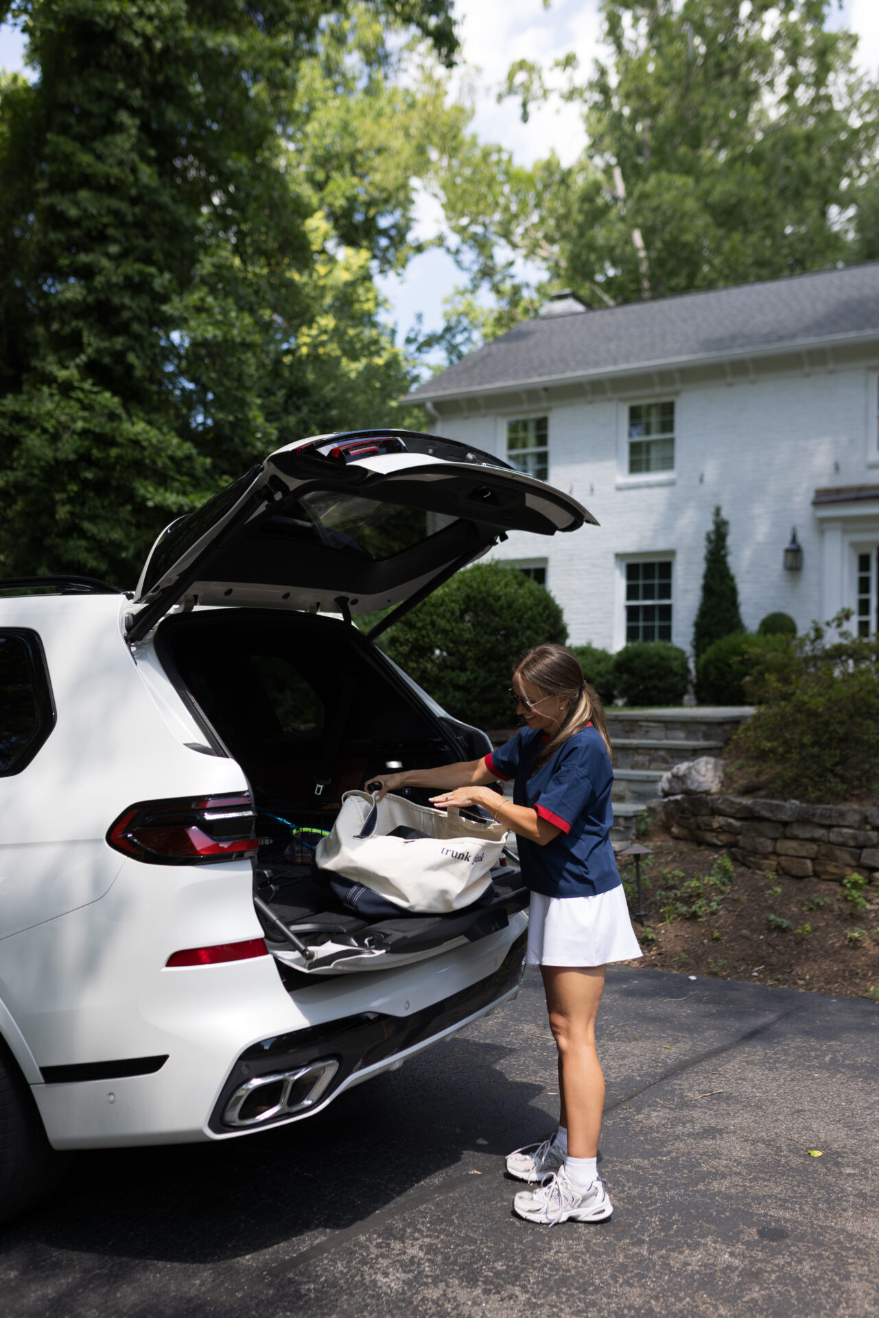 TeriLyn Adams packing her car wearing navy tuckernuck top and white skirt for a sideline casual mom outfit.