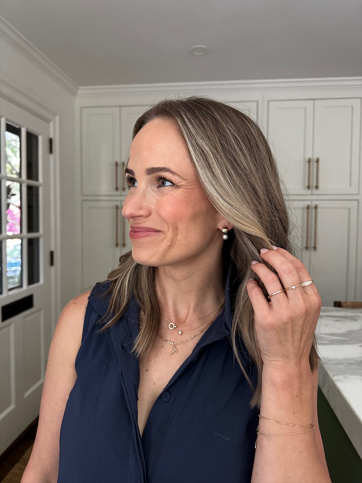 TeriLyn Adams in navy top wearing Mejuri pearl drop earrings layered gold necklaces and gold rings
