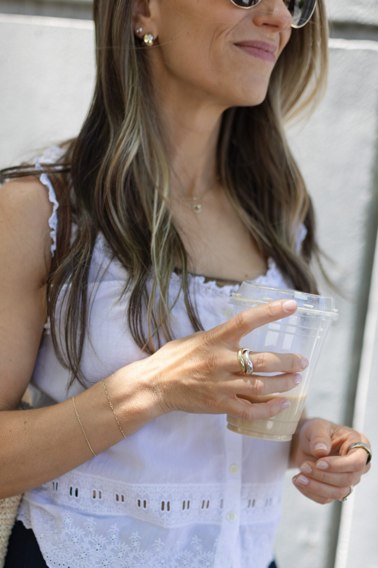 TeriLyn Adams in white eyelet top holding iced coffee wearing Mejuri rings and gold chain bracelet