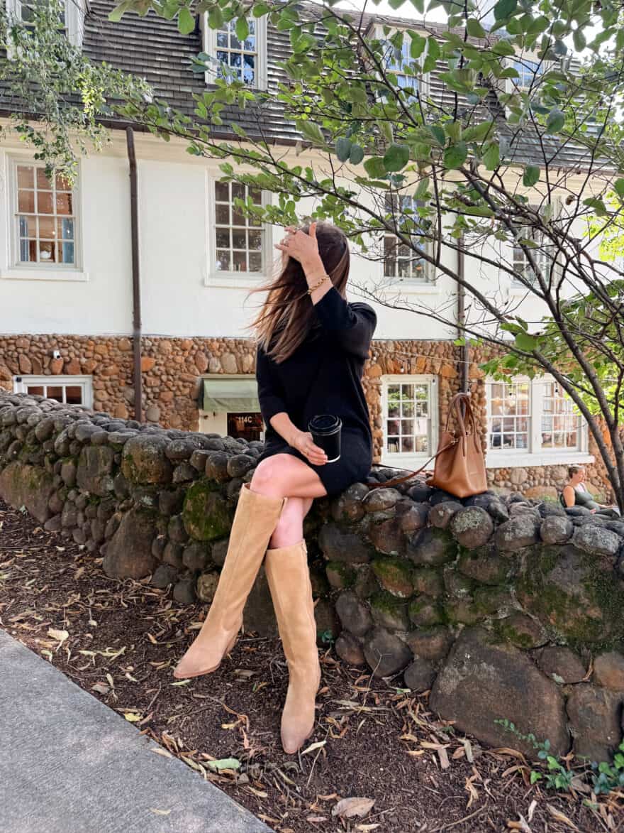 Woman sitting on wall in black dress and knee high boots