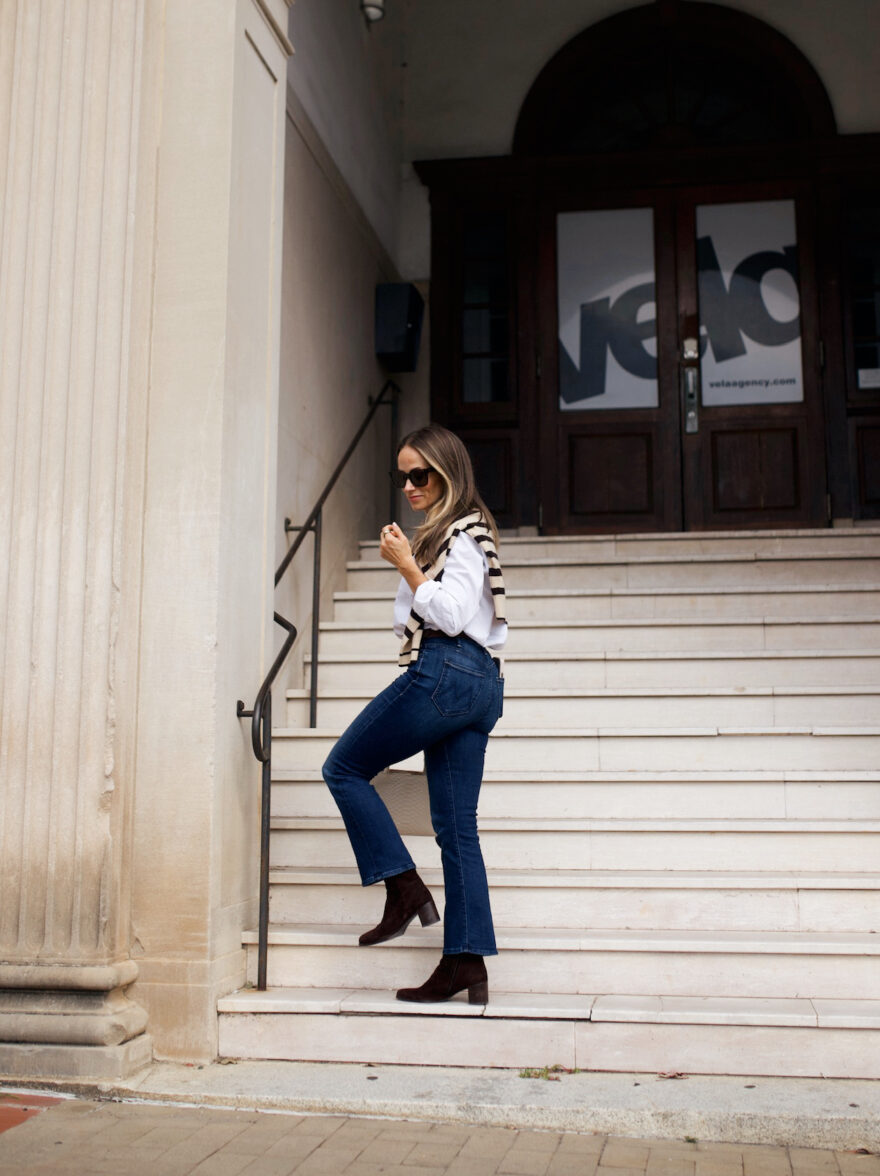 Woman walking up stairs in jeans, Tuckernuck boots, and a white button up shirt with a draped sweater