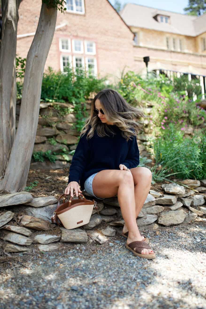 Woman in her 40s wearing denim shorts and a black sweatshirt with brown sandals