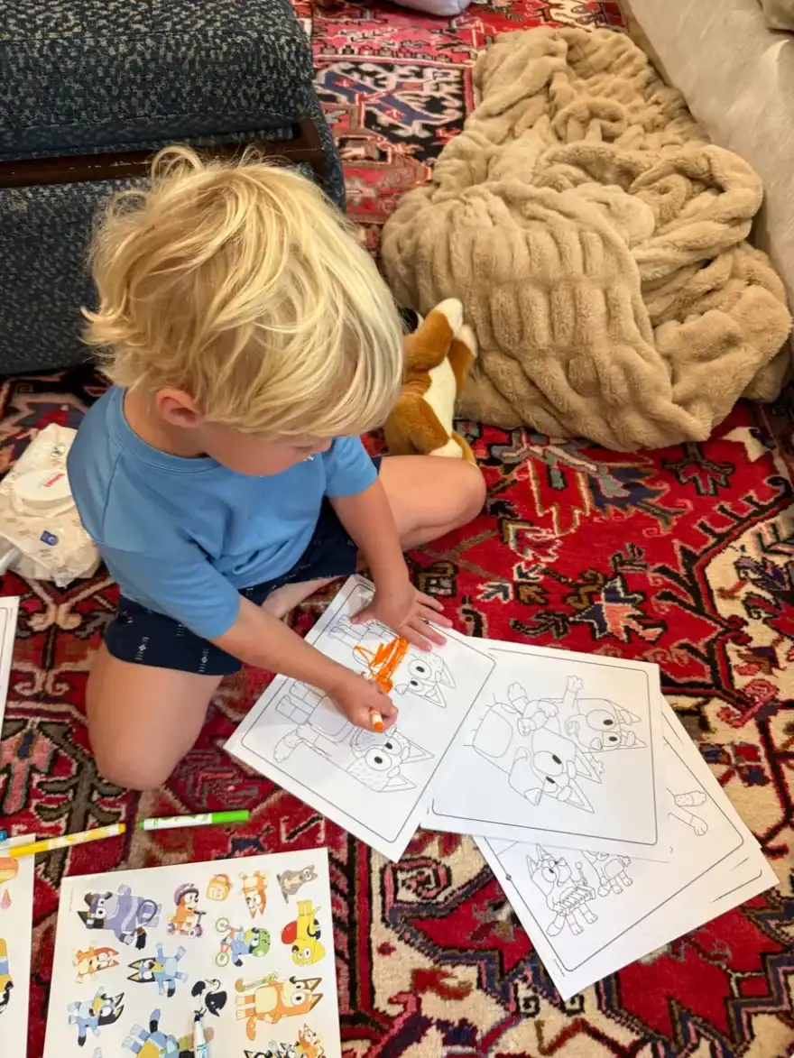 Little boy sitting on rug coloring pictures