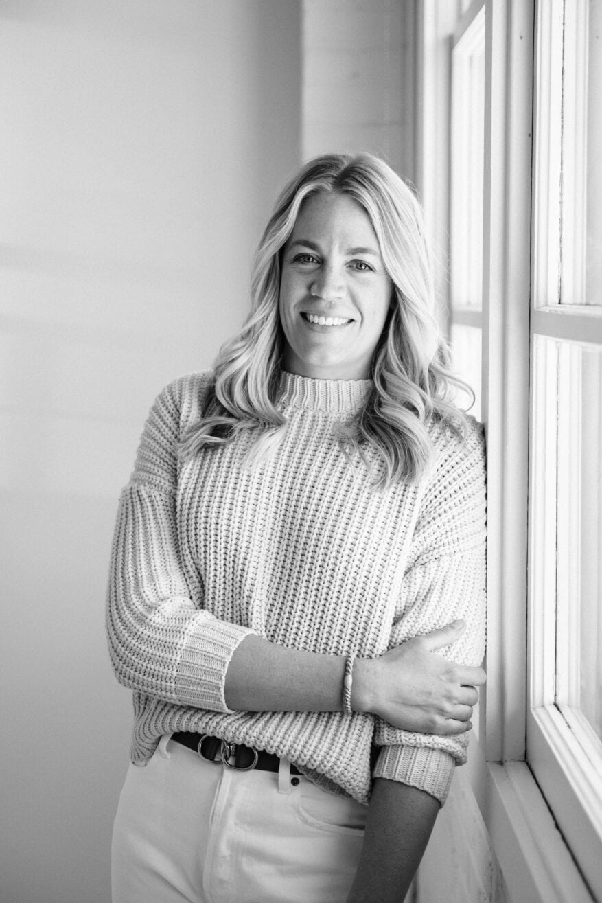 woman standing by window in sweater and white denim