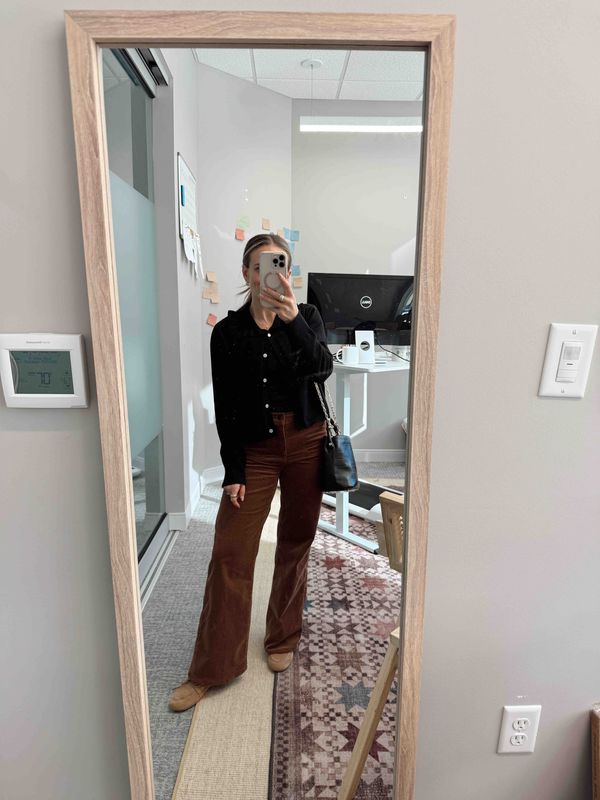 TeriLyn Adams wearing a black cardigan, brown corduroy pants, and loafers with a crossbody bag