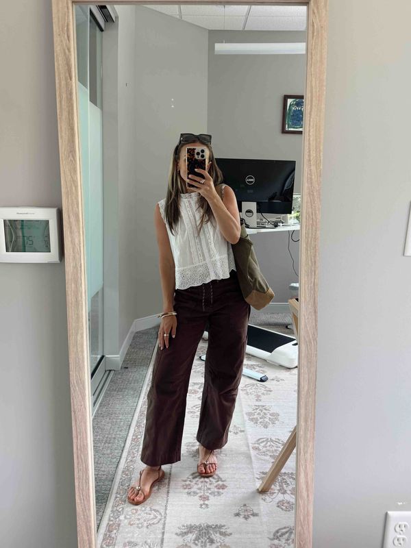 TeriLyn Adams wearing a white lace top, brown utility pants, and sandals with an olive bag