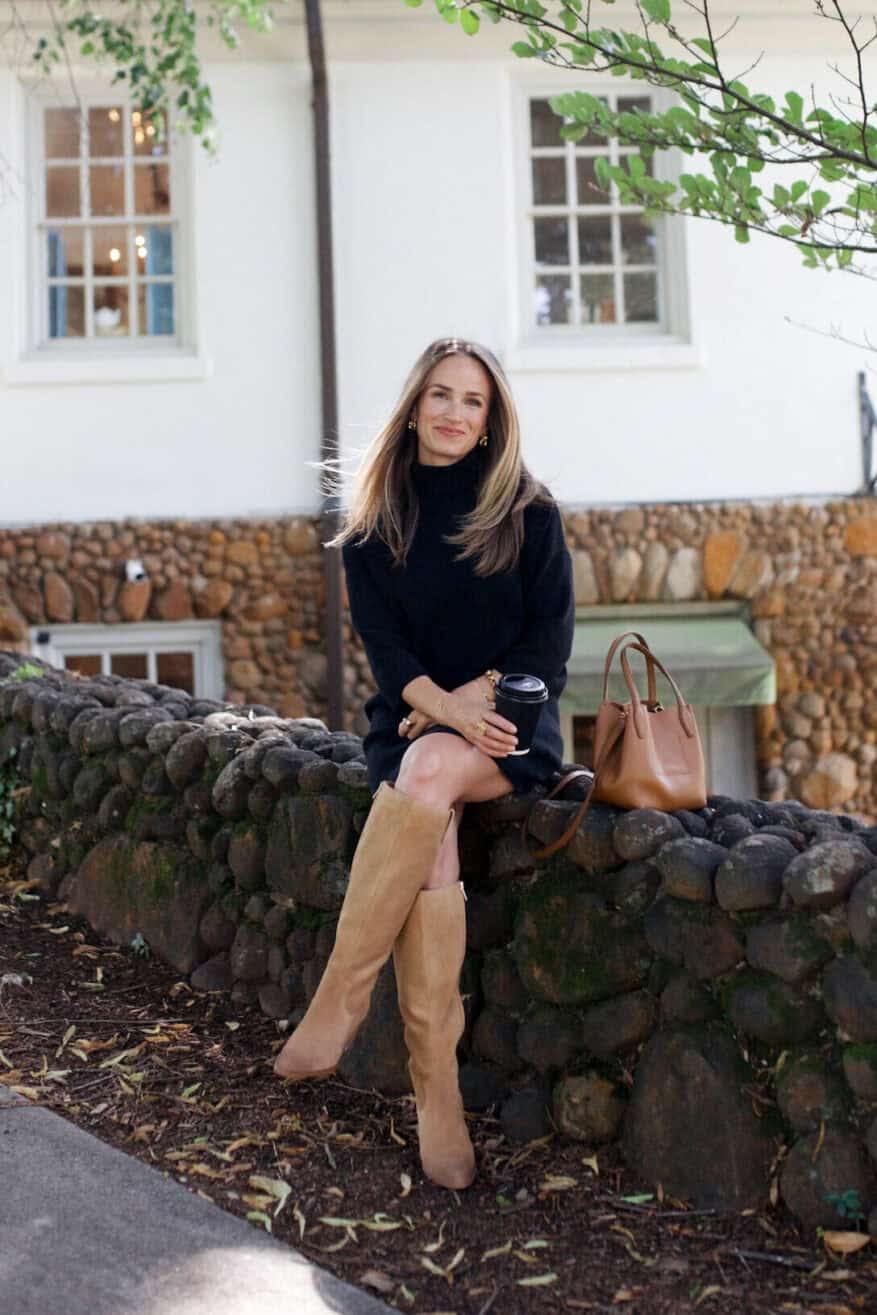 Woman sitting on rock wall wearing a black turtleneck sweater dress