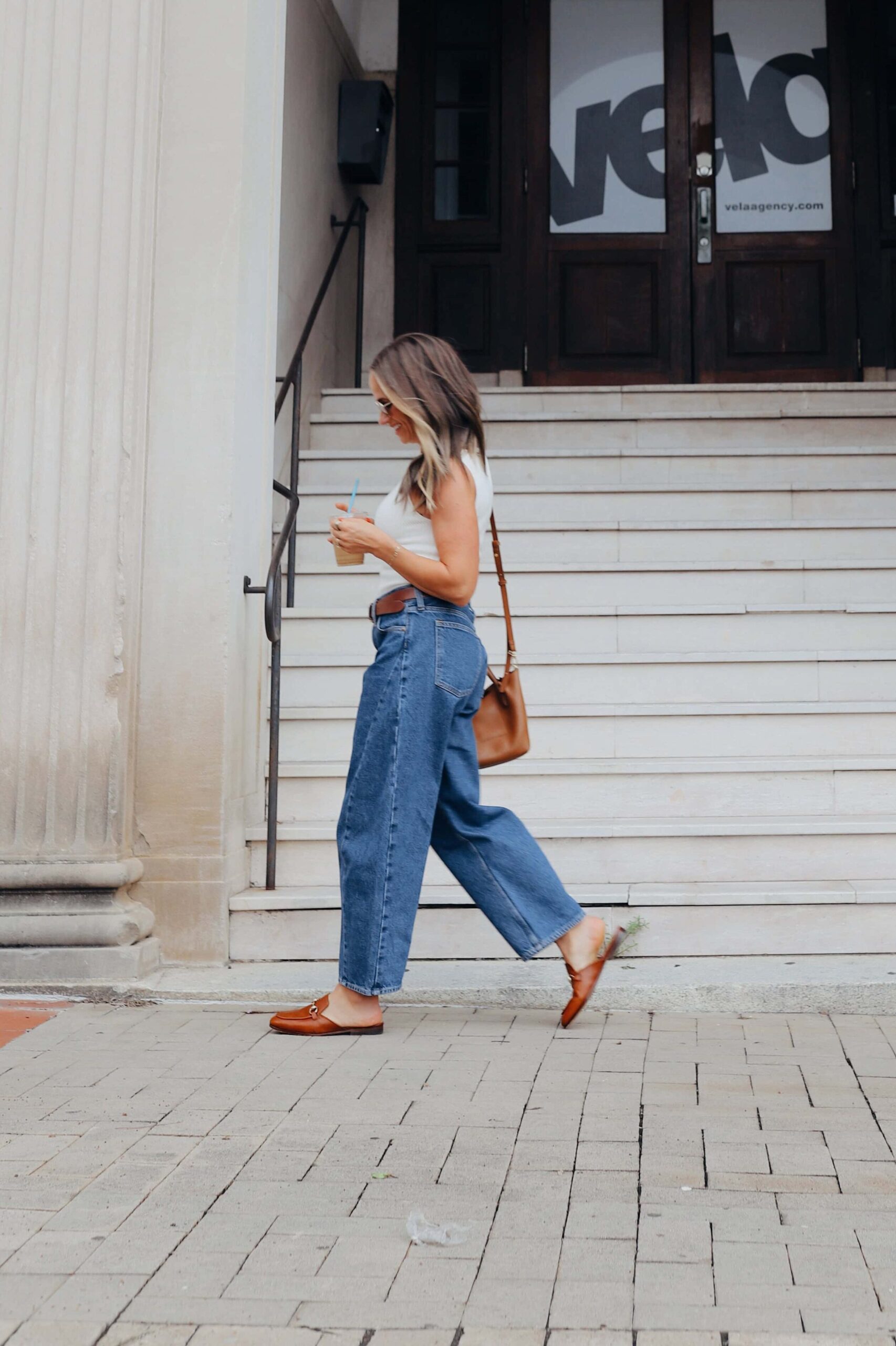 Woman walking in Abercrombie barrel jean with white top and leather purse