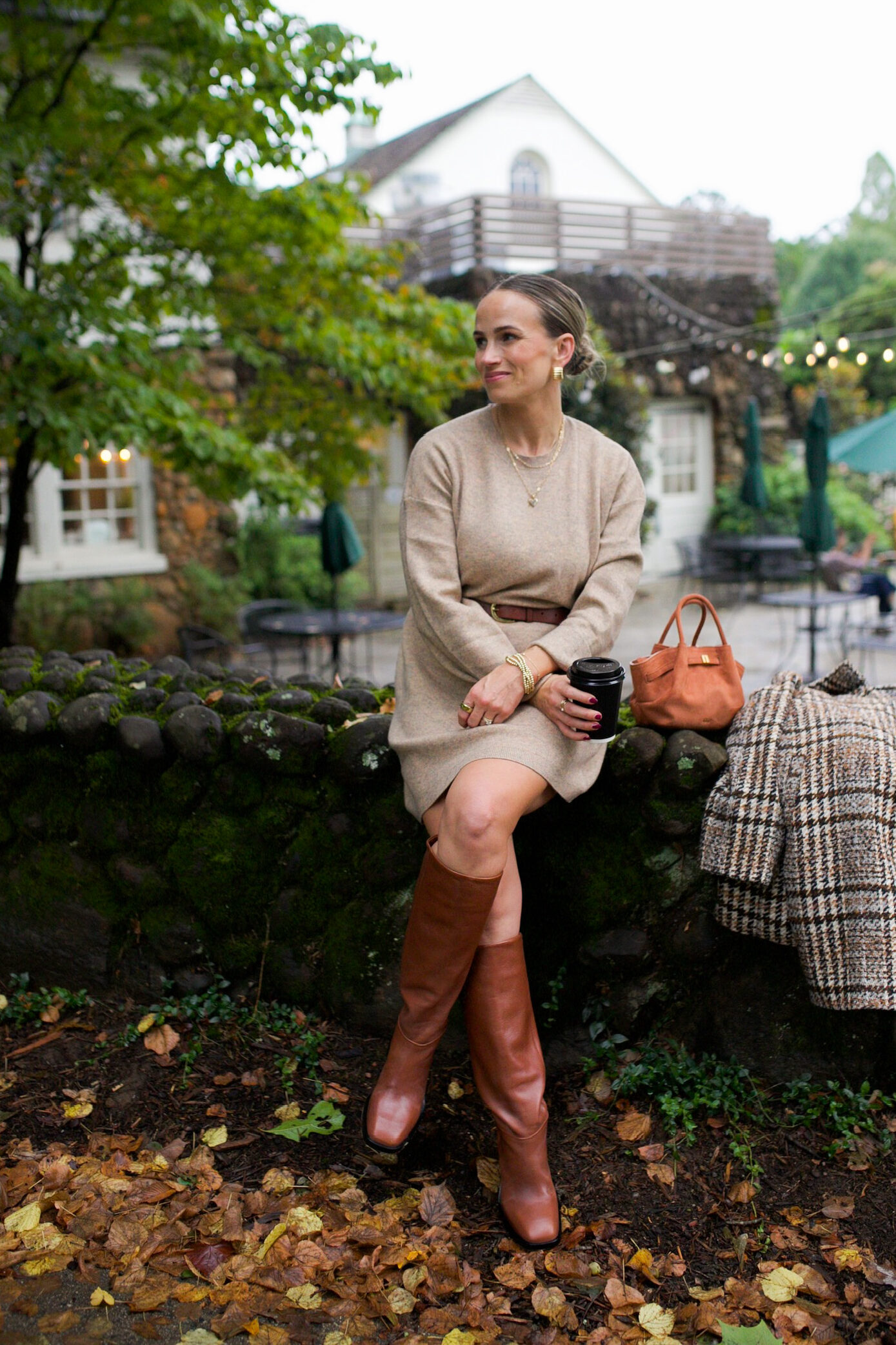 Woman sitting in a sweater dress with a belt, and tall boots