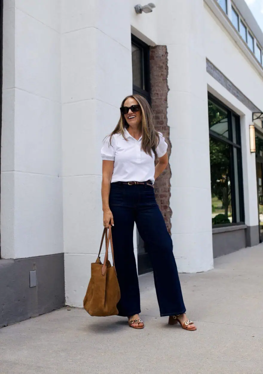 Woman wearing dark wide leg jeans with a white top and leather purse