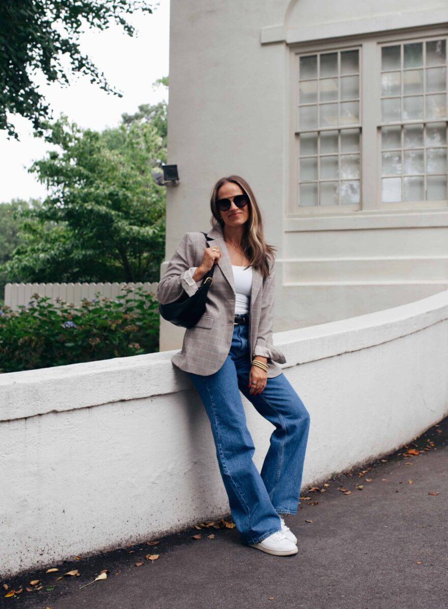 Woman sitting on wall while wearing a blazer and jeans