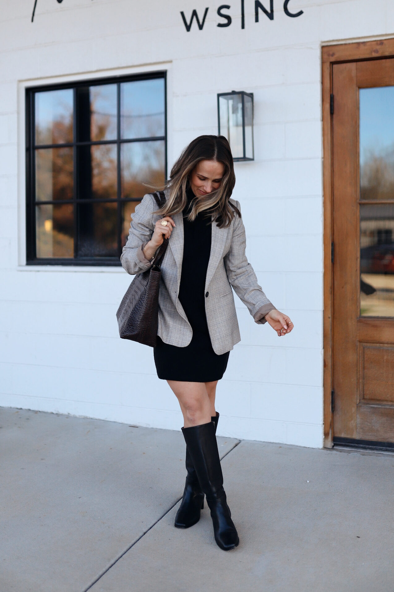 Woman standing outside a shop wearing a sweater dress with a blazer blazer