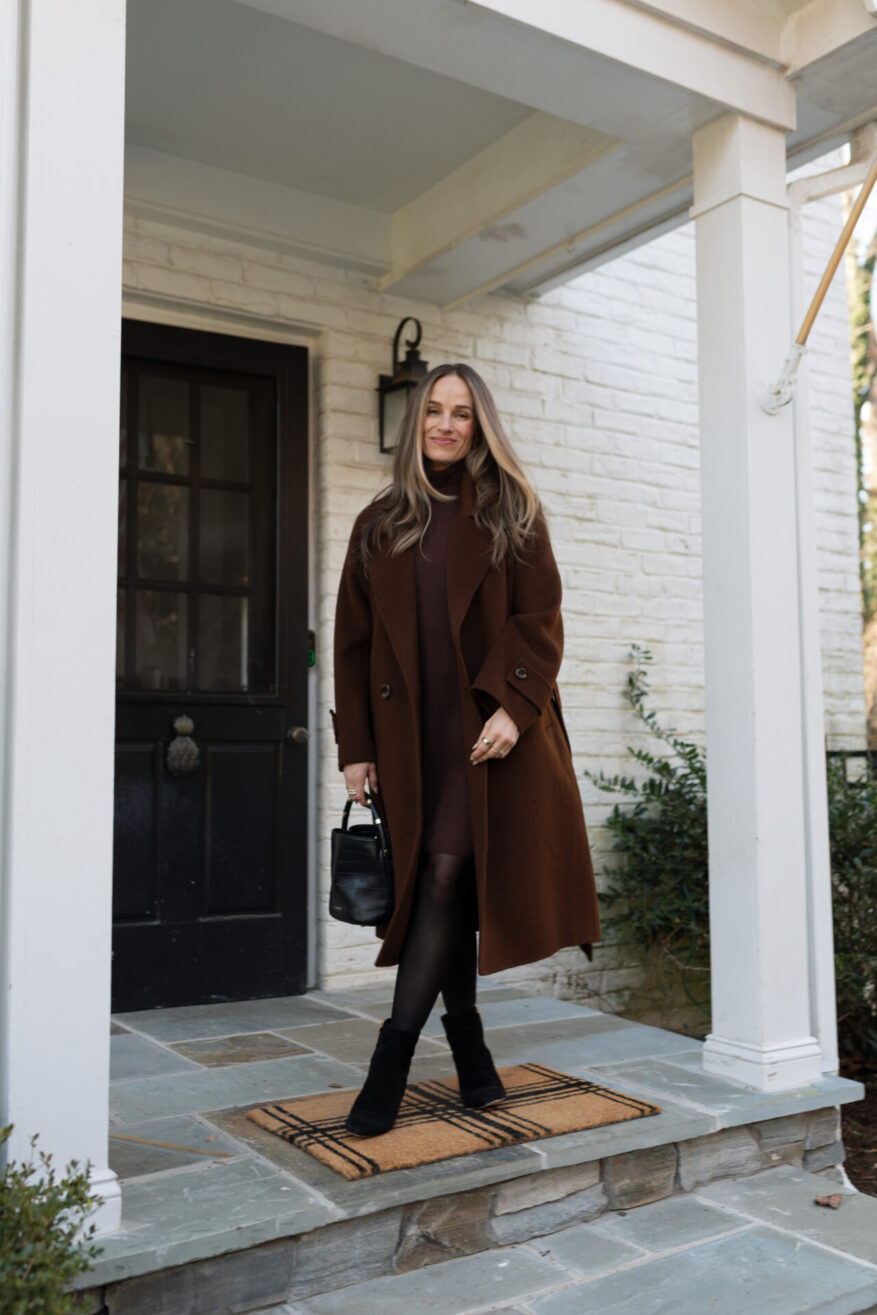 TeriLyn Adams wearing a belted brown wool coat with black tights and black suede ankle boots on a porch