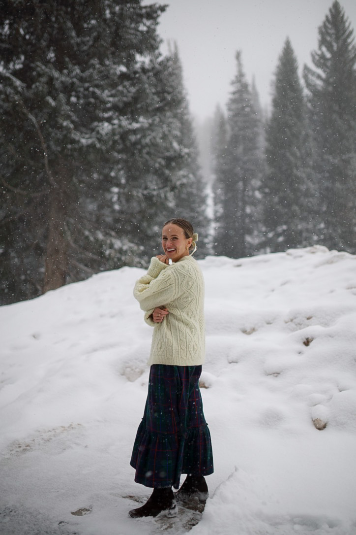 TeriLyn Adams wearing a cream cable-knit sweater, tartan tiered maxi skirt and dark boots in the snow
