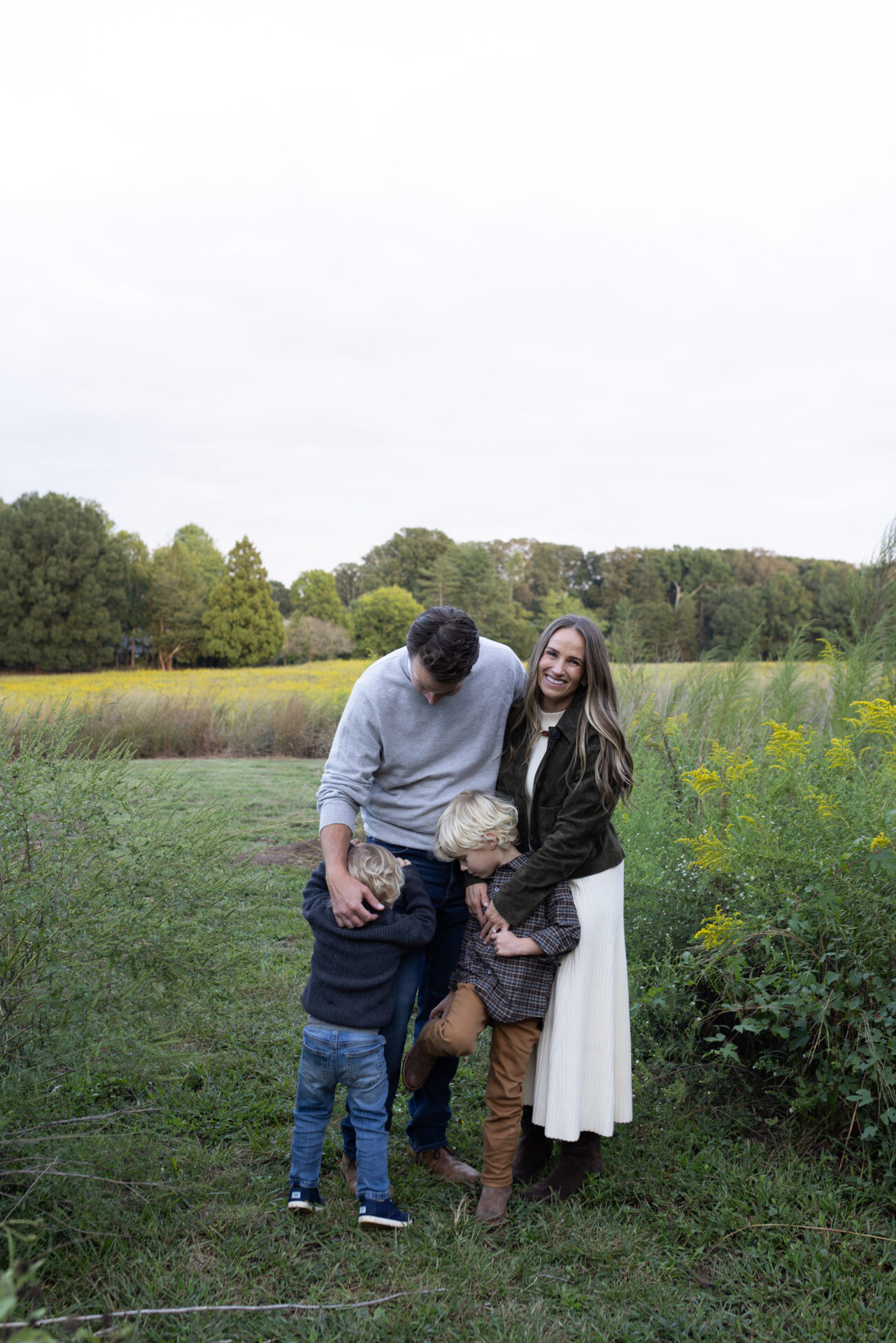 TeriLyn Adams and her family in a fall field, with her in an olive suede jacket, cream knit skirt and brown suede boots