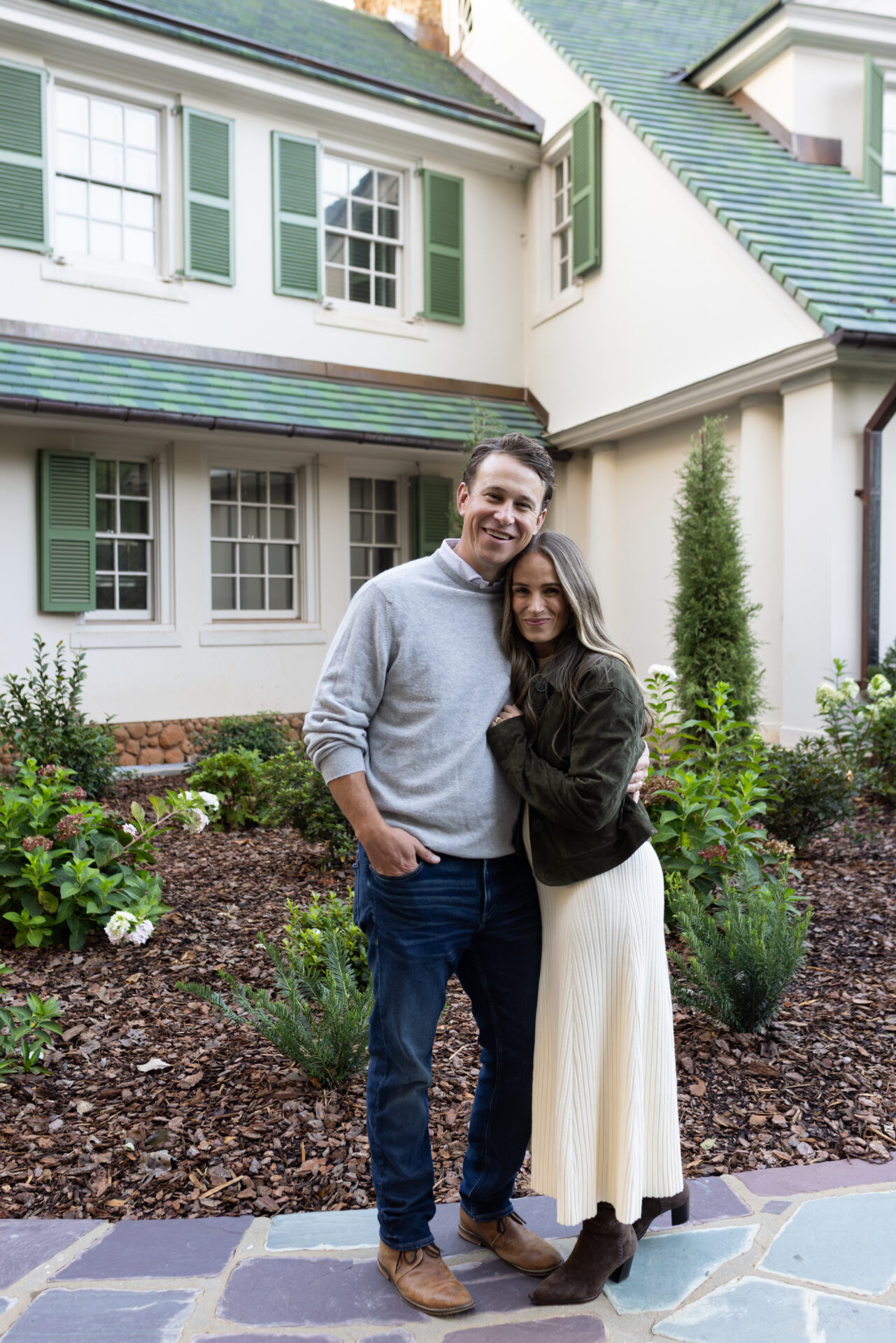 TeriLyn Adams and her husband outside, with her in an olive suede jacket, cream knit midi skirt and brown suede boots