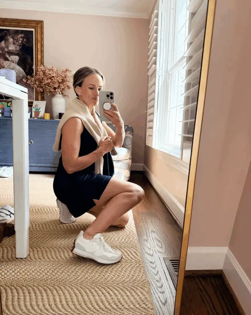 Woman taking a selfie in an athletic dress and tennis shoes with a sweater around her shoulder