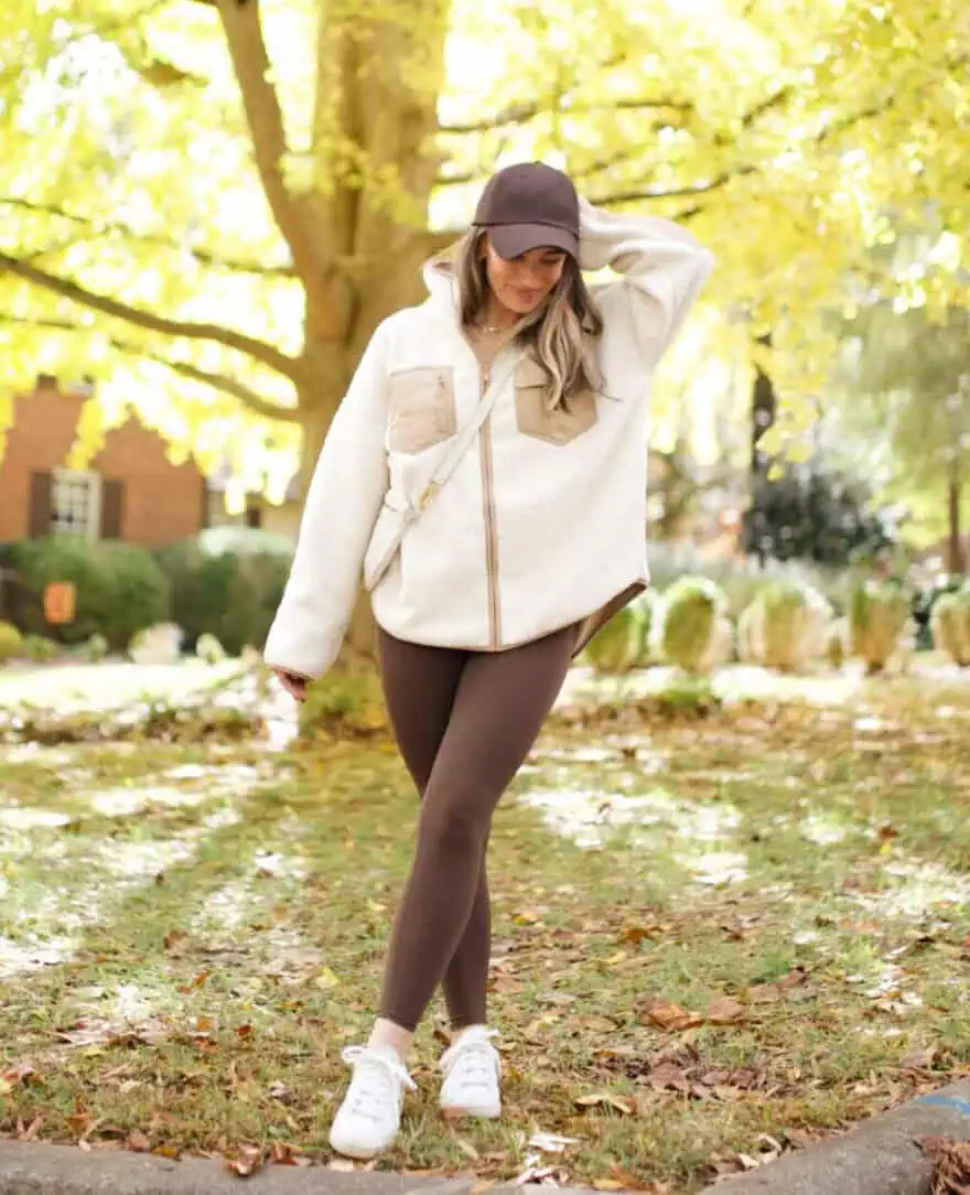 Woman standing outside while wearing leggings, a jacket, hat, and tennis shoes