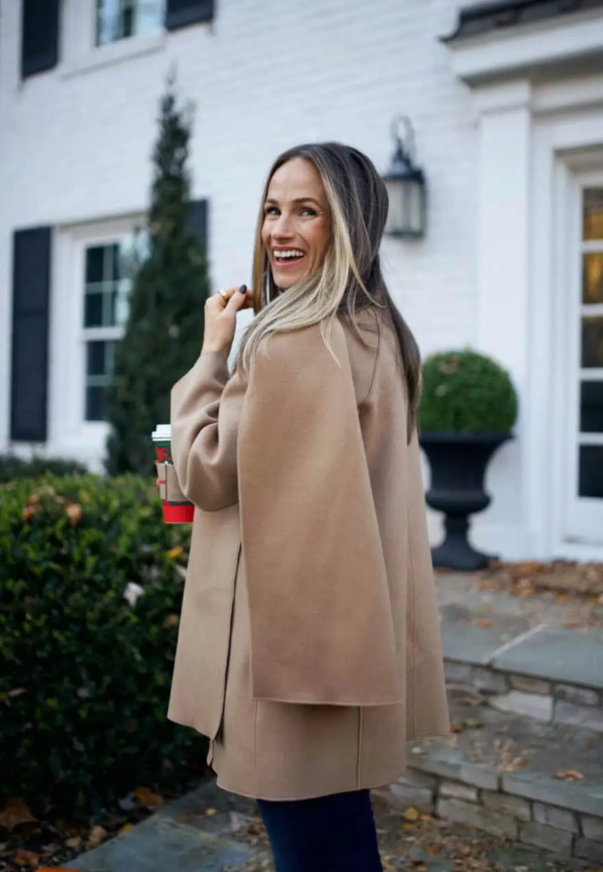 Woman standing outside wearing a scarf jacket and holding a coffee