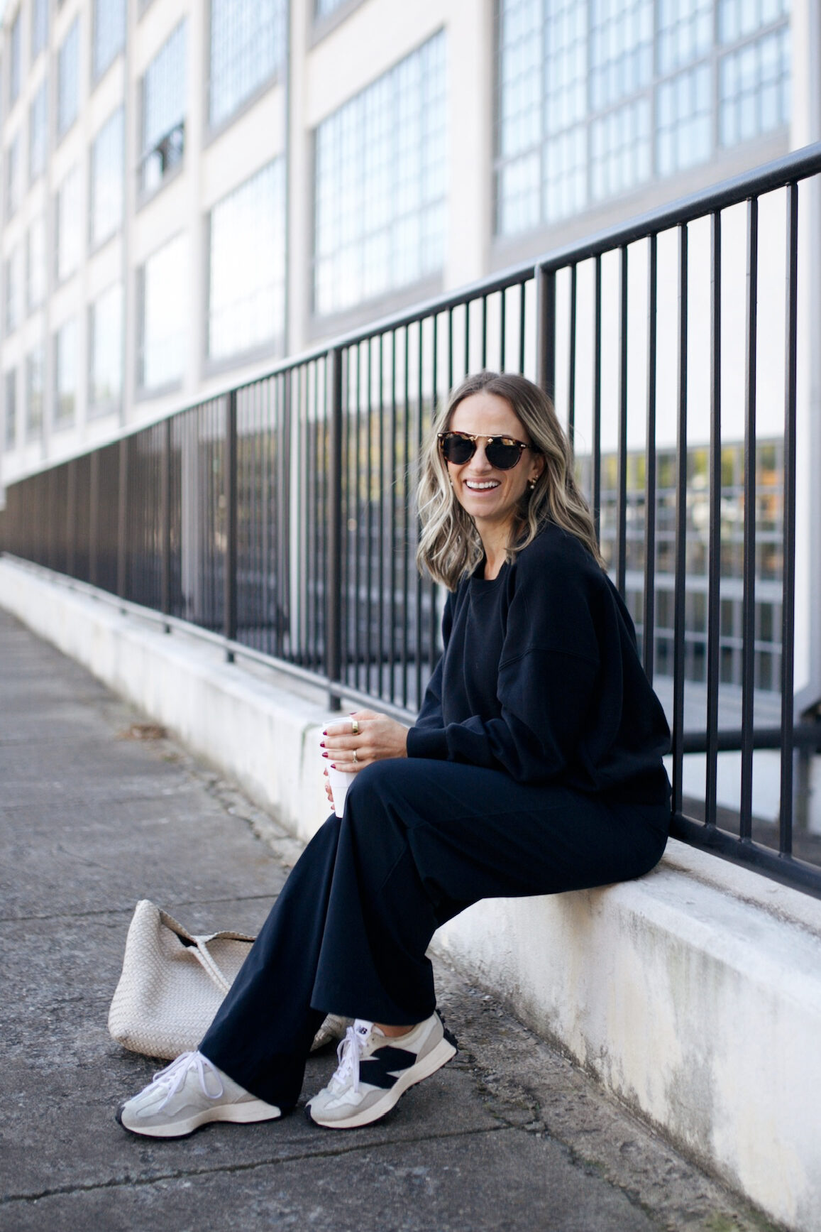 Woman sitting and wearing wide leg matching pants set in black with New Balance sneakers