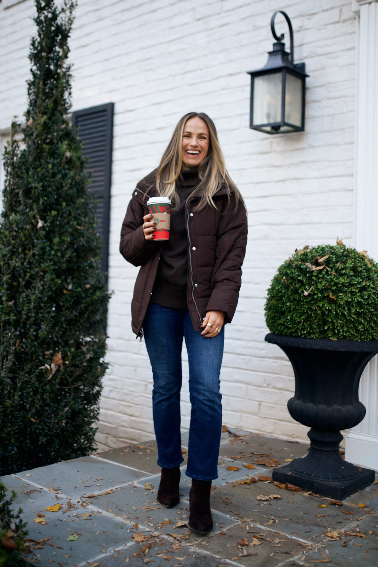 Woman wearing jeans with booties, a turtleneck, and a puffer jacket while standing on porch