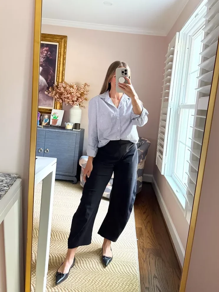 Woman taking a selfie while wearing trousers and a button down shirt with pointed flats