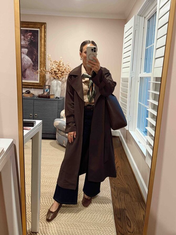 Woman taking a selfie while wearing a trench coat over a button-down and trousers with flats