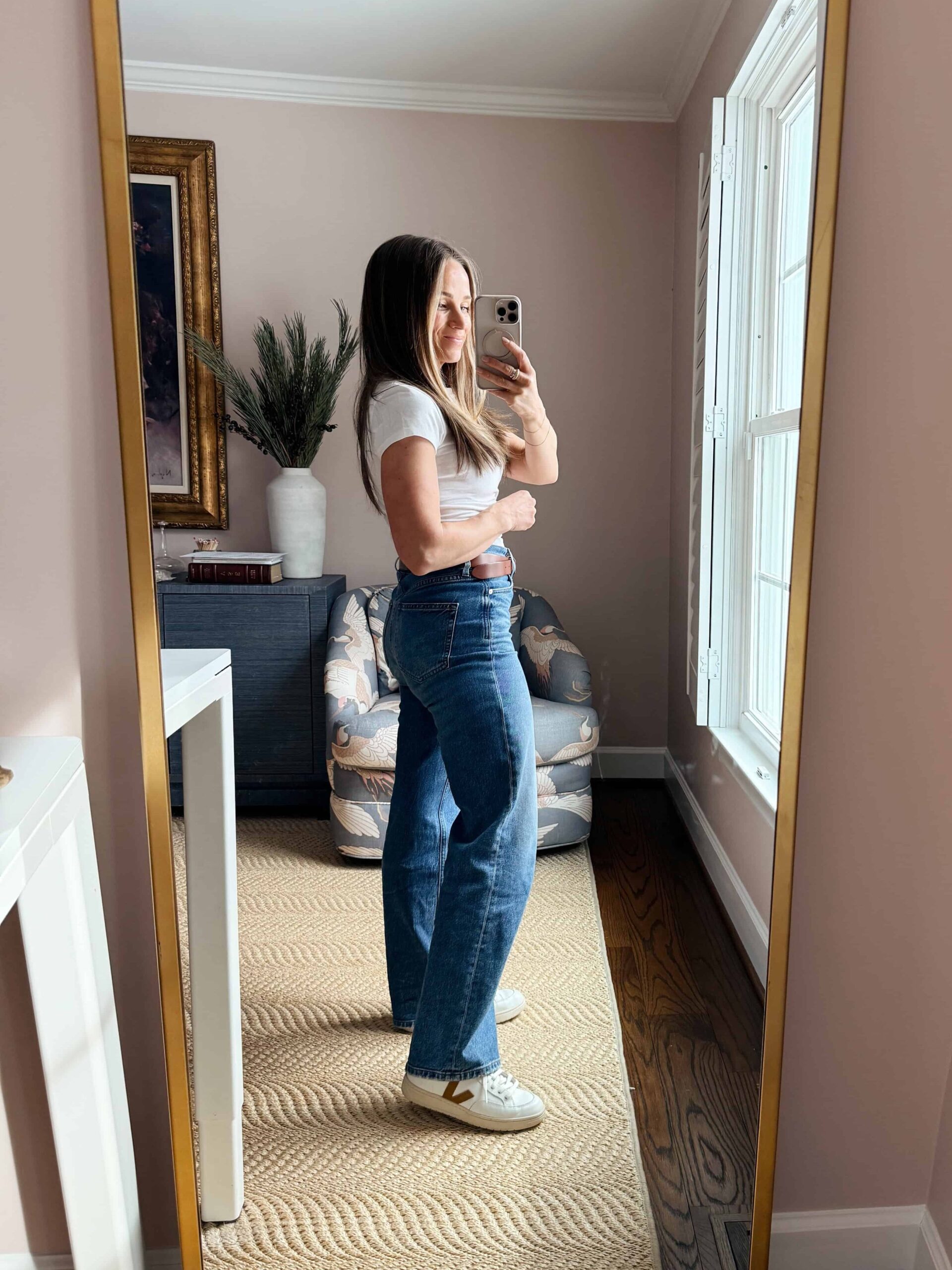 Woman showing side view of wide leg jeans with a tucked in, fitted white top