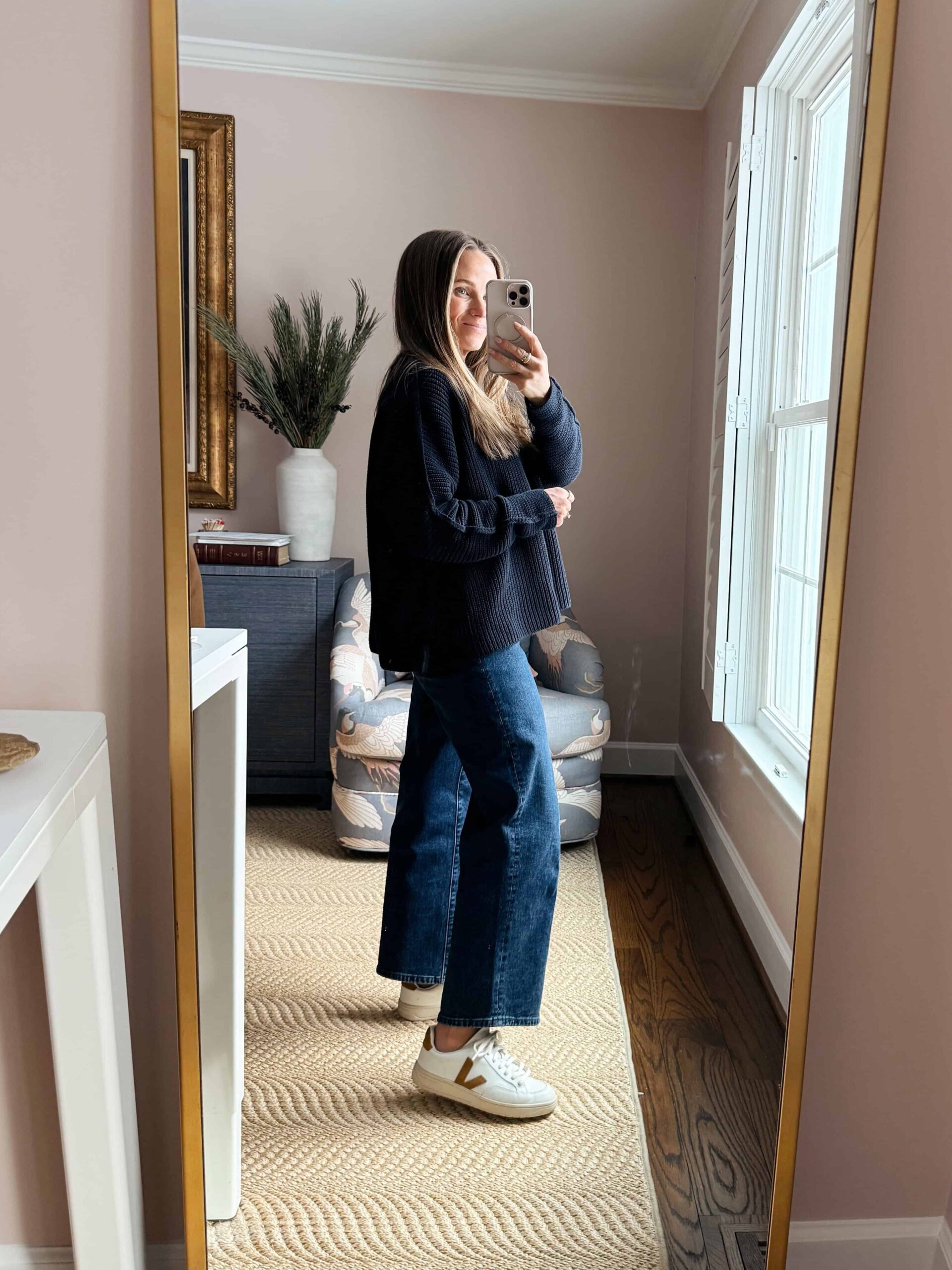 Woman showing side view of cropped wide-leg jeans with oversized navy sweater and sneakers