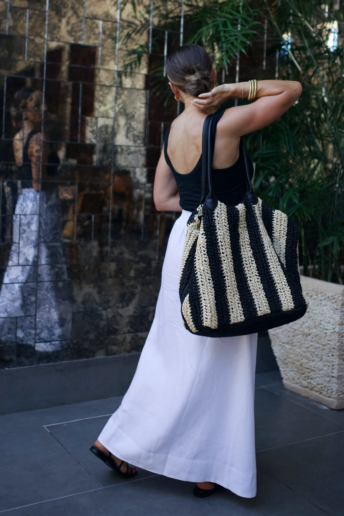 Woman checking reflection in white skirt, black top, and bag