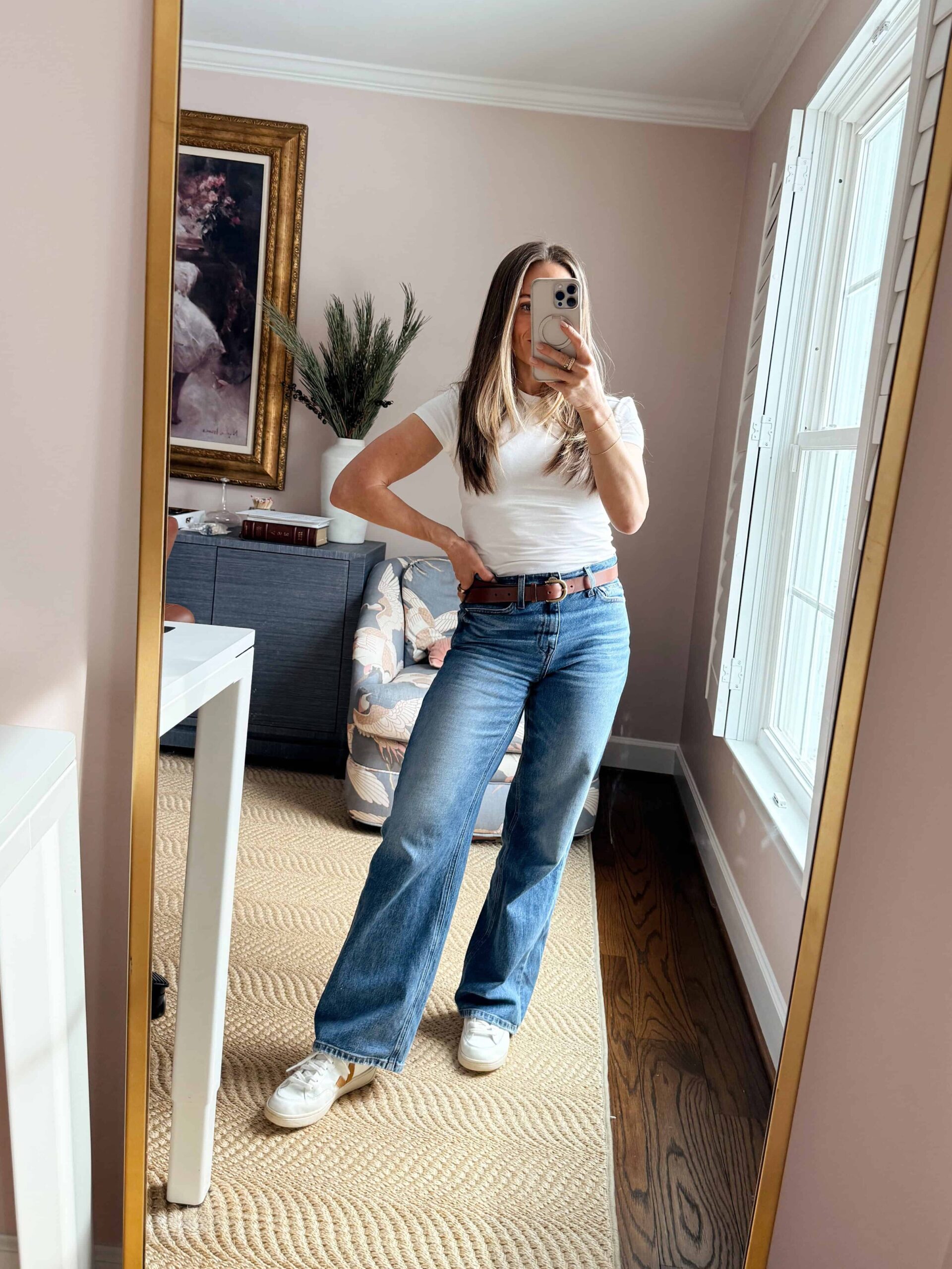 Woman taking picture wearing wide leg jeans with a tucked in, fitted white top